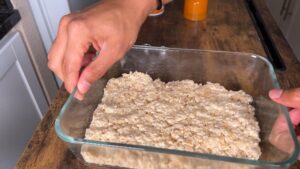 A Hand Pressing the Rice Krispie Mixture Into a Glass Baking Dish to Set and Cool