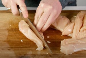 A chef's hands expertly slice a raw chicken