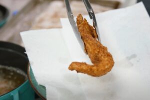 Crispy fried chicken finger removed from hot oil using tongs