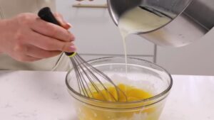 Pouring Warm Milk Into a Bowl of Whisked Egg Yolks to Make the Bavarian Cream for Charlotte Russe