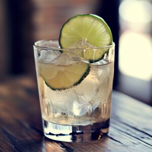 A glass filled with ice, a fizzy cocktail, and lime slices on a wooden table