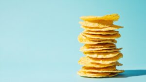 A stack of golden tortilla chips against a bright blue background