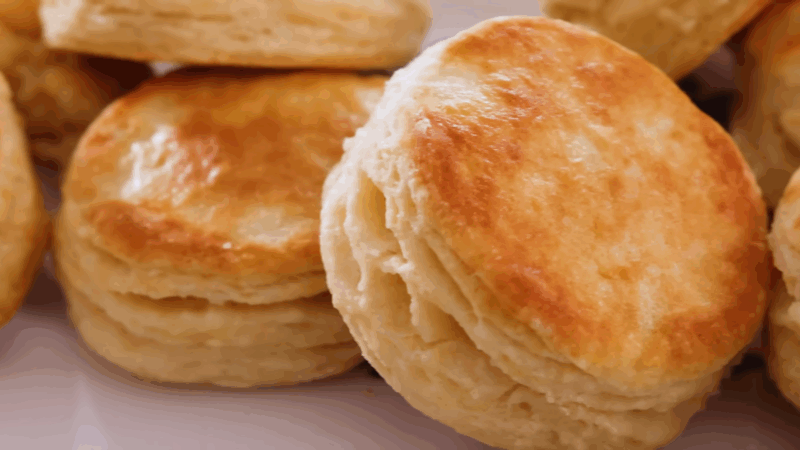 Fluffy buttermilk biscuits with golden tops stacked on a plate