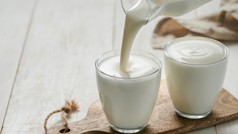 Pouring leftover buttermilk into a glass on a wooden board, ready to use in recipes