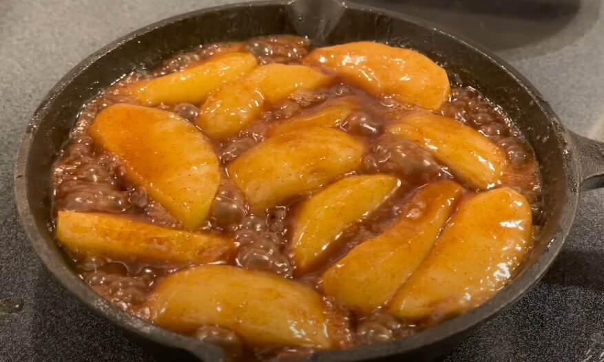 A cast-iron skillet filled with caramelized apple slices, glistening with a rich syrup