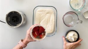 A person prepares to blend fresh strawberries in a small blender cup