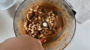 Roasted peanuts being mixed into date caramel in a food processor