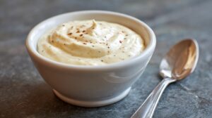 Small white bowl of creamy horseradish sauce sprinkled with pepper, next to a spoon