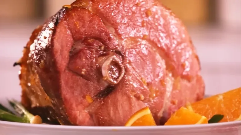 Baked butt portion ham resting on a platter with a glossy glaze and sliced citrus nearby