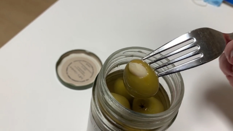 A fork lifts a garlic-stuffed olive from an open jar on a table