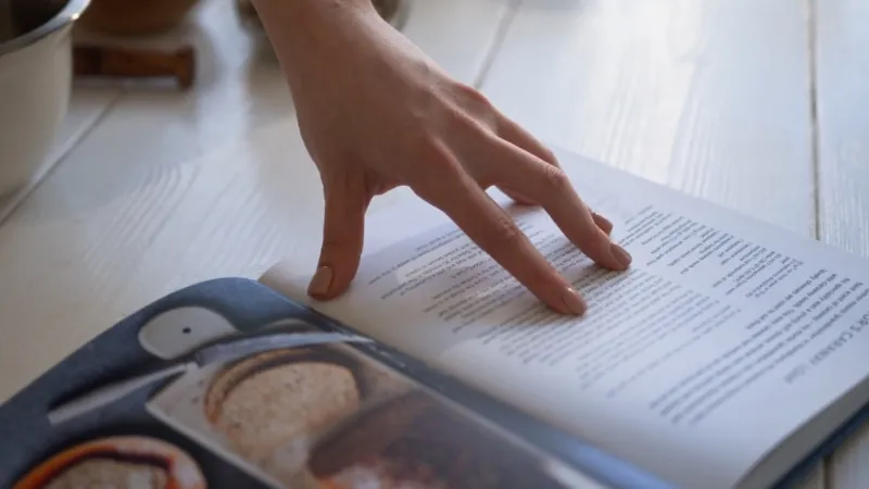 Hand flips pages of a printed book as recipes into a cookbook take shape