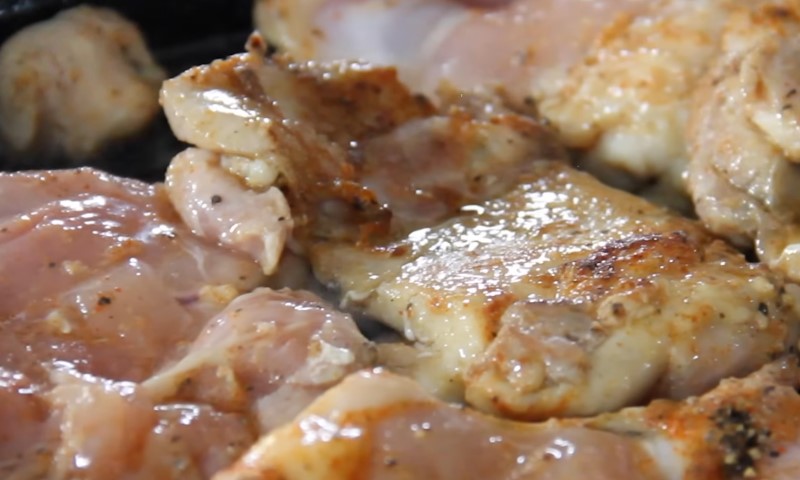 Close-up of seasoned, lightly browned chicken pieces sizzling in a pan