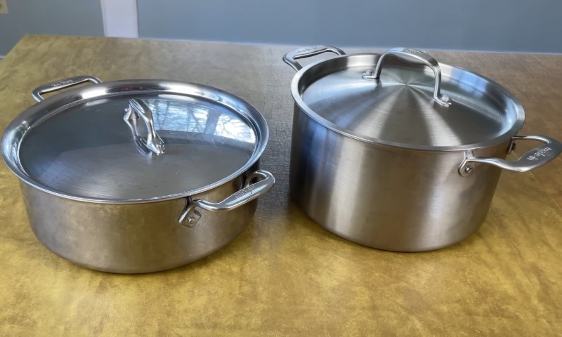 Two stainless steel pots with lids on a wooden surface