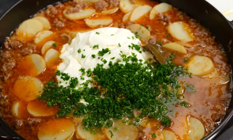 A hearty stew in a black pot with sliced potatoes, ground meat, and a rich