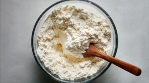 Glass bowl filled with flour mixture and thick yogurt being combined with a wooden spoon