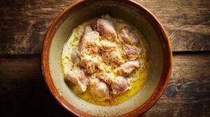 Raw chicken pieces soaking in seasoned buttermilk in a bowl