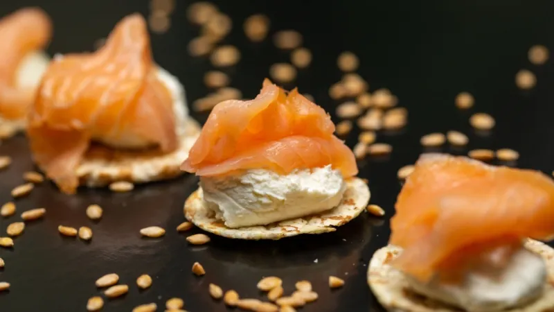 Crackers topped with cream cheese and smoked salmon with sesame seeds scattered around