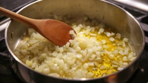 Diced onions cooking in a pot with oil, being stirred with a wooden spoon