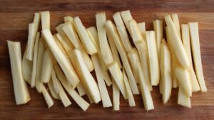 Raw parsnips cut into evenly sized sticks on a wooden cutting board