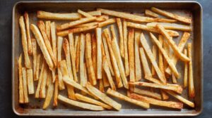 Roasted parsnip sticks spread out on a baking tray with lightly browned edges