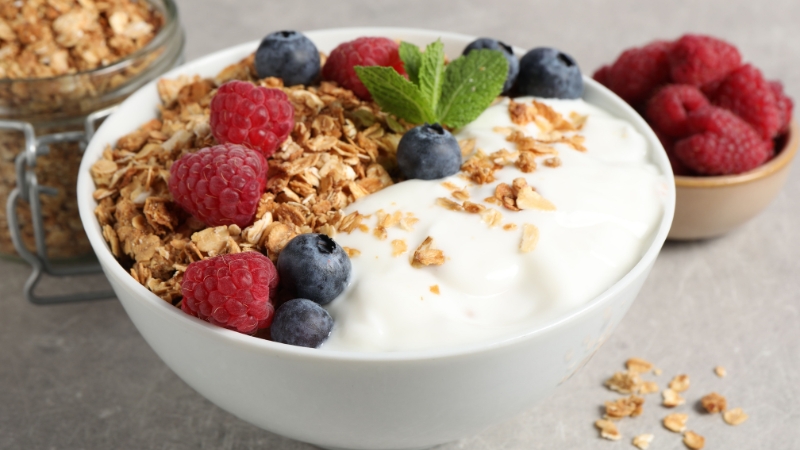 Bowl of yogurt topped with granola, raspberries, and blueberries