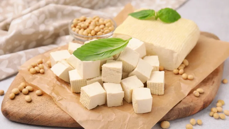 Tofu cubes on a cutting board with soybeans and basil leaves