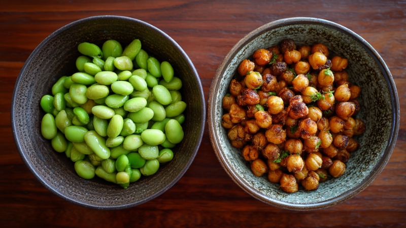Bowls of edamame and roasted chickpeas placed side by side on a wooden table