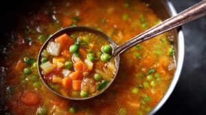 Ladle scooping vegetable soup with peas, carrots, and diced vegetables from a pot of broth