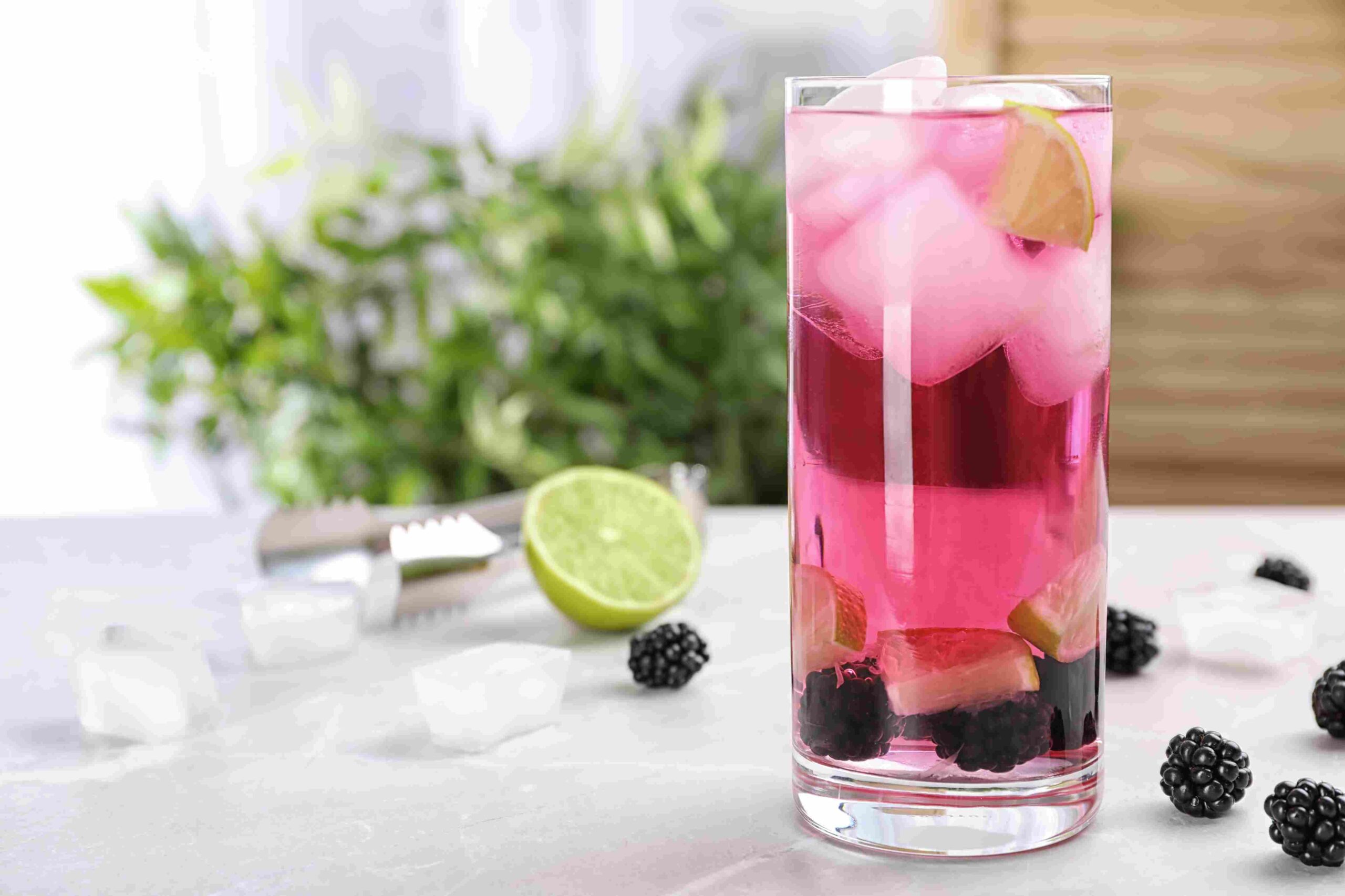Tall glass of pink blackberry drink with ice, lime slices, and fresh berries at the bottom