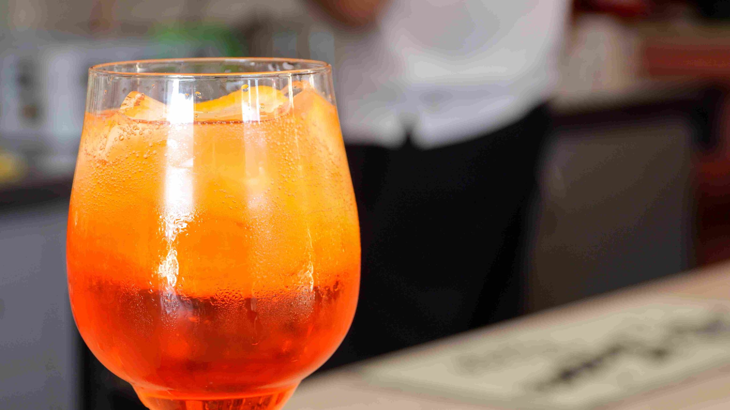 Glass of orange-colored citrus drink with ice on a bar counter
