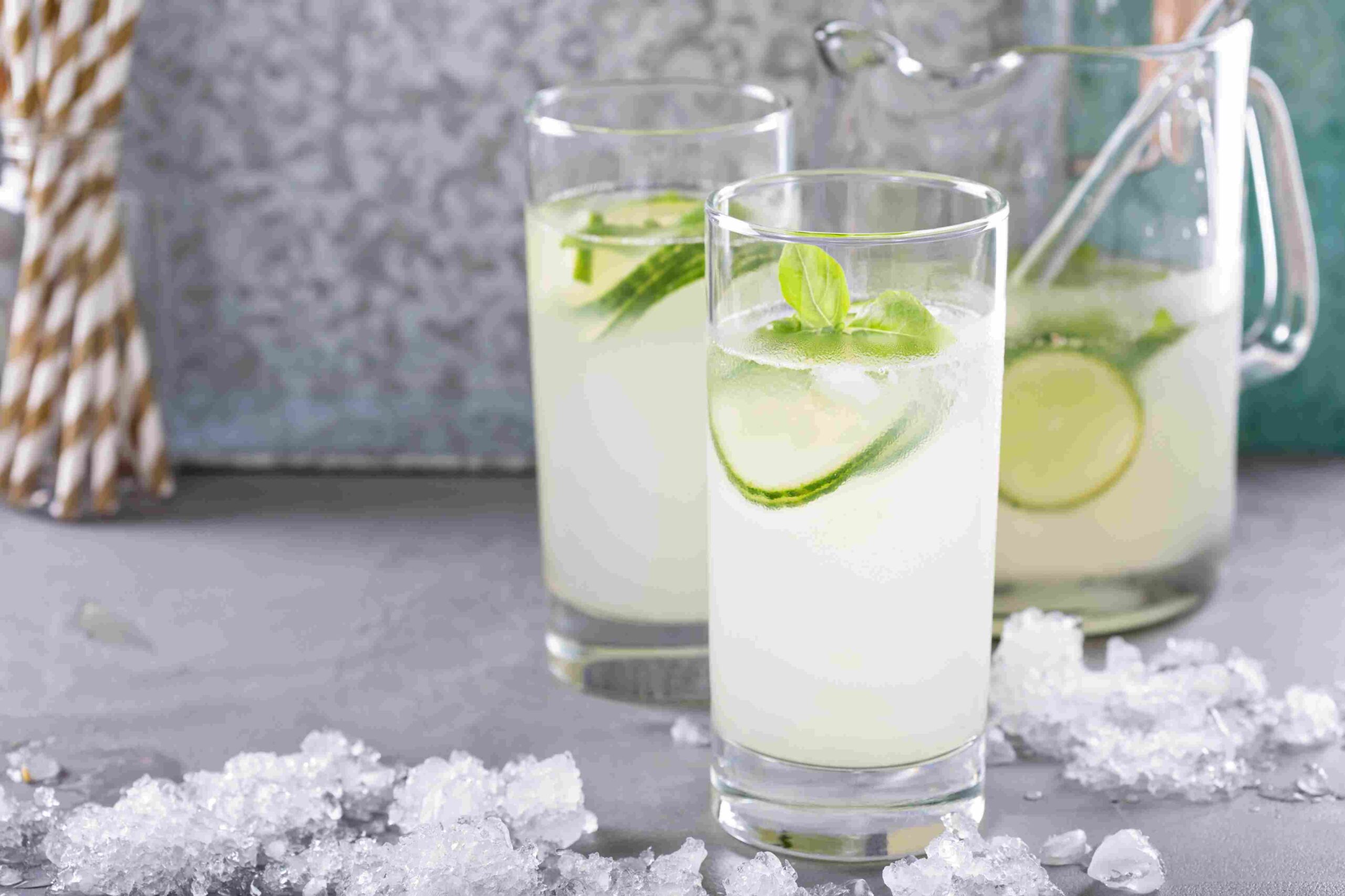 Tall glasses of pale green cucumber drink with mint leaves and lime slices over ice