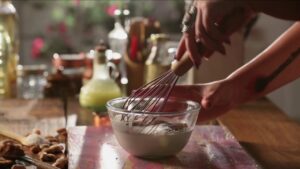 A person whisking cocoa powder into whole milk in a glass bowl while preparing chocolate phirni