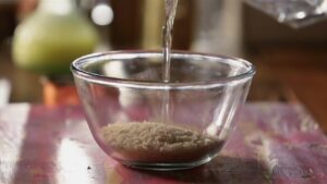 Water being poured into a glass bowl containing basmati rice as the first step in preparing chocolate phirni